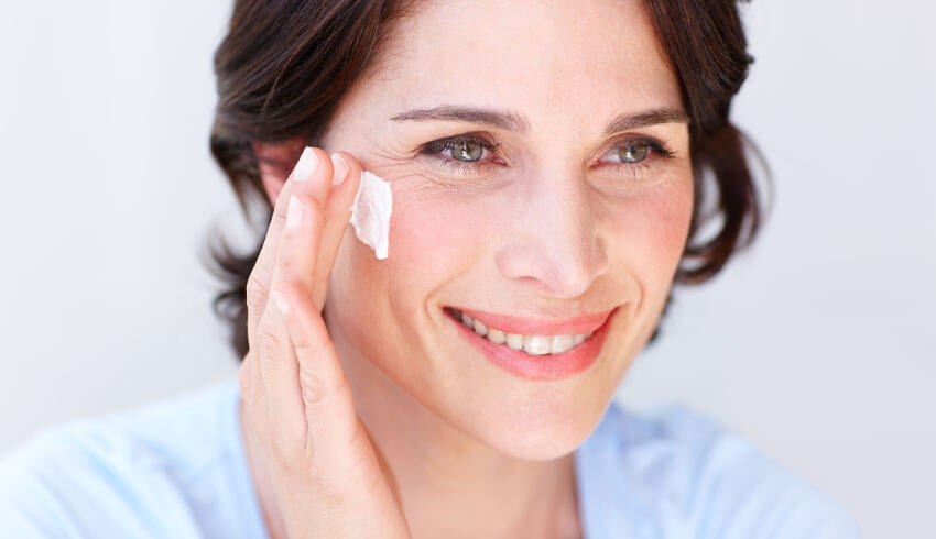 A woman smiling as she applies cream to her face